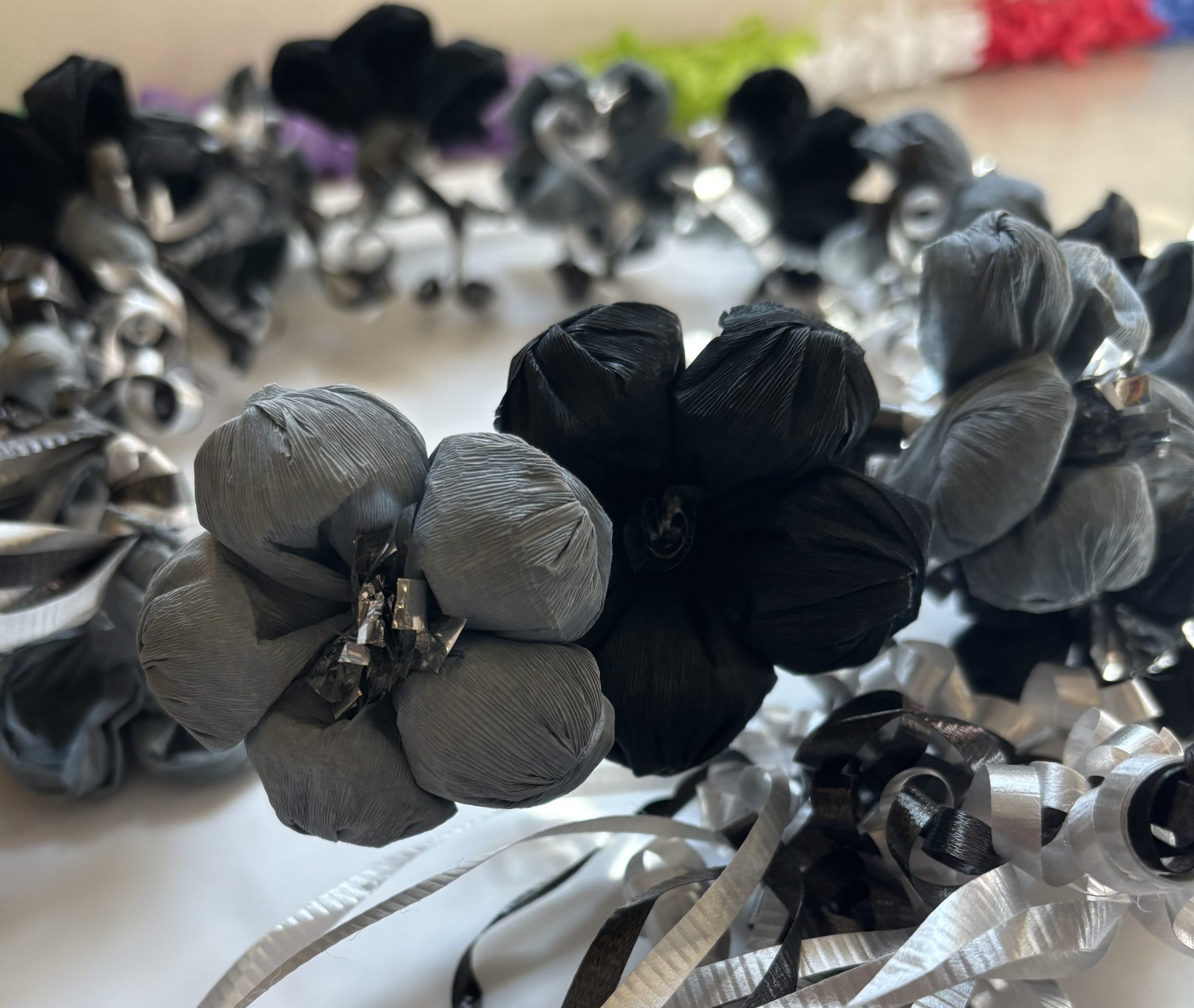 Close-up of a paper flower corona in San Antonio Spurs colors, black and silver crepe paper blossoms with curled silver ribbon, arranged in a circular wreath.
